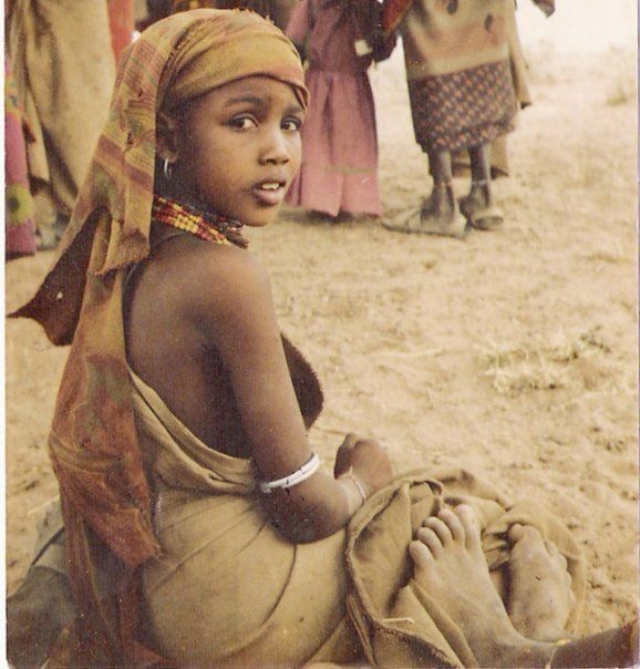 A young girl wearing a head scarf is sitting on the ground