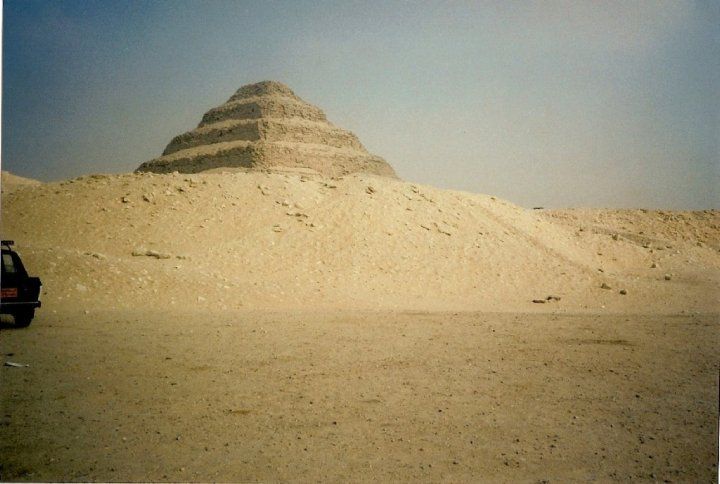 A car is parked in front of a pyramid in the desert