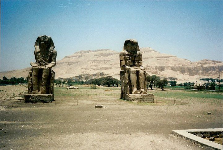 Two statues in a field with mountains in the background
