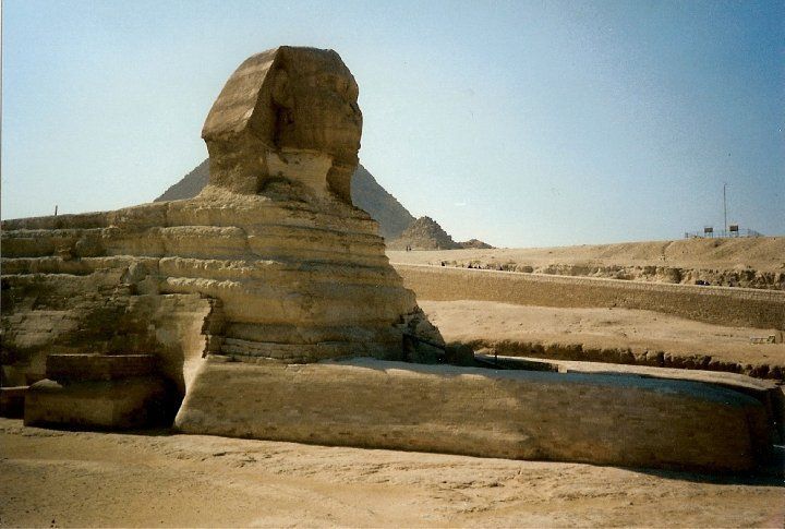 A statue of a sphinx in the desert with a pyramid in the background
