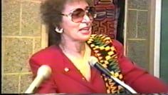 A woman wearing sunglasses is standing in front of a microphone.