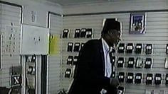 A man in a suit and tie is standing in a room with a wall of cell phones.