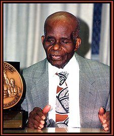 A man in a suit and tie stands in front of a trophy that says bee