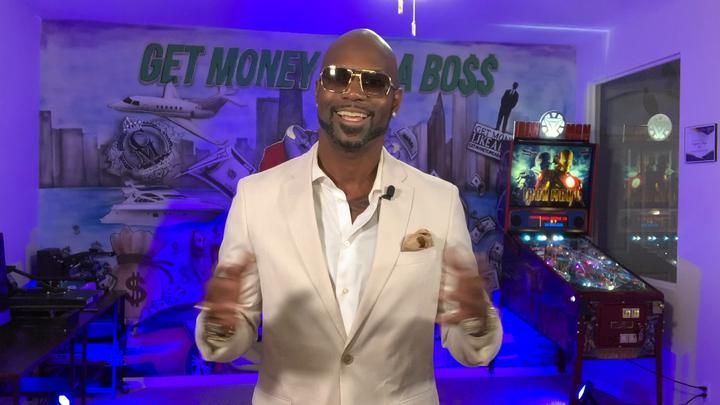 A man in a suit and sunglasses is standing in front of a pinball machine.