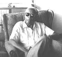 A man wearing sunglasses is sitting in a chair in a black and white photo.