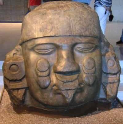 A statue of a man 's head is sitting on top of a pile of sand.