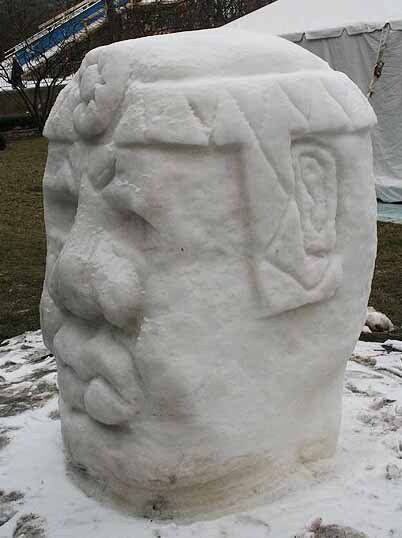 A large snow sculpture of a man 's head is sitting in the snow.