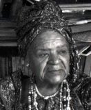 A black and white photo of an elderly woman wearing a turban and necklaces.
