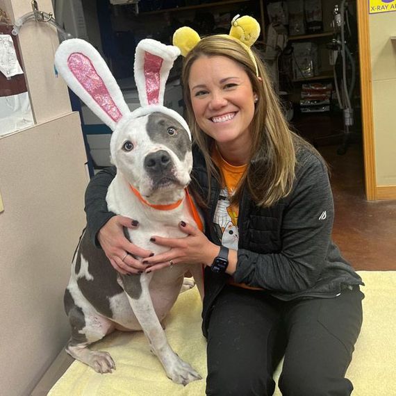 A woman is sitting next to a dog wearing bunny ears