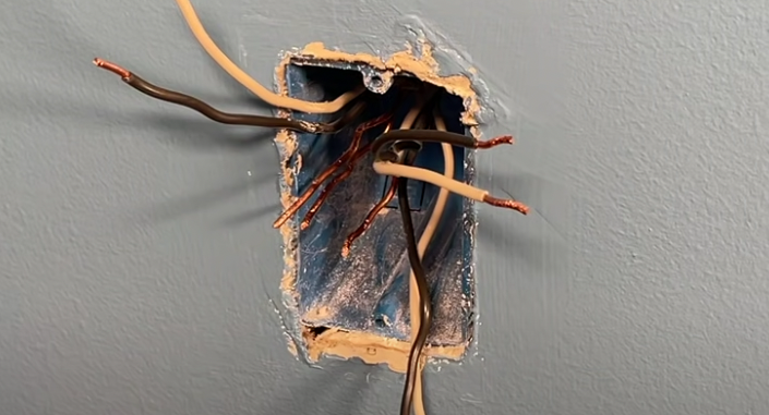 A hole in a wall with wires coming out of it.