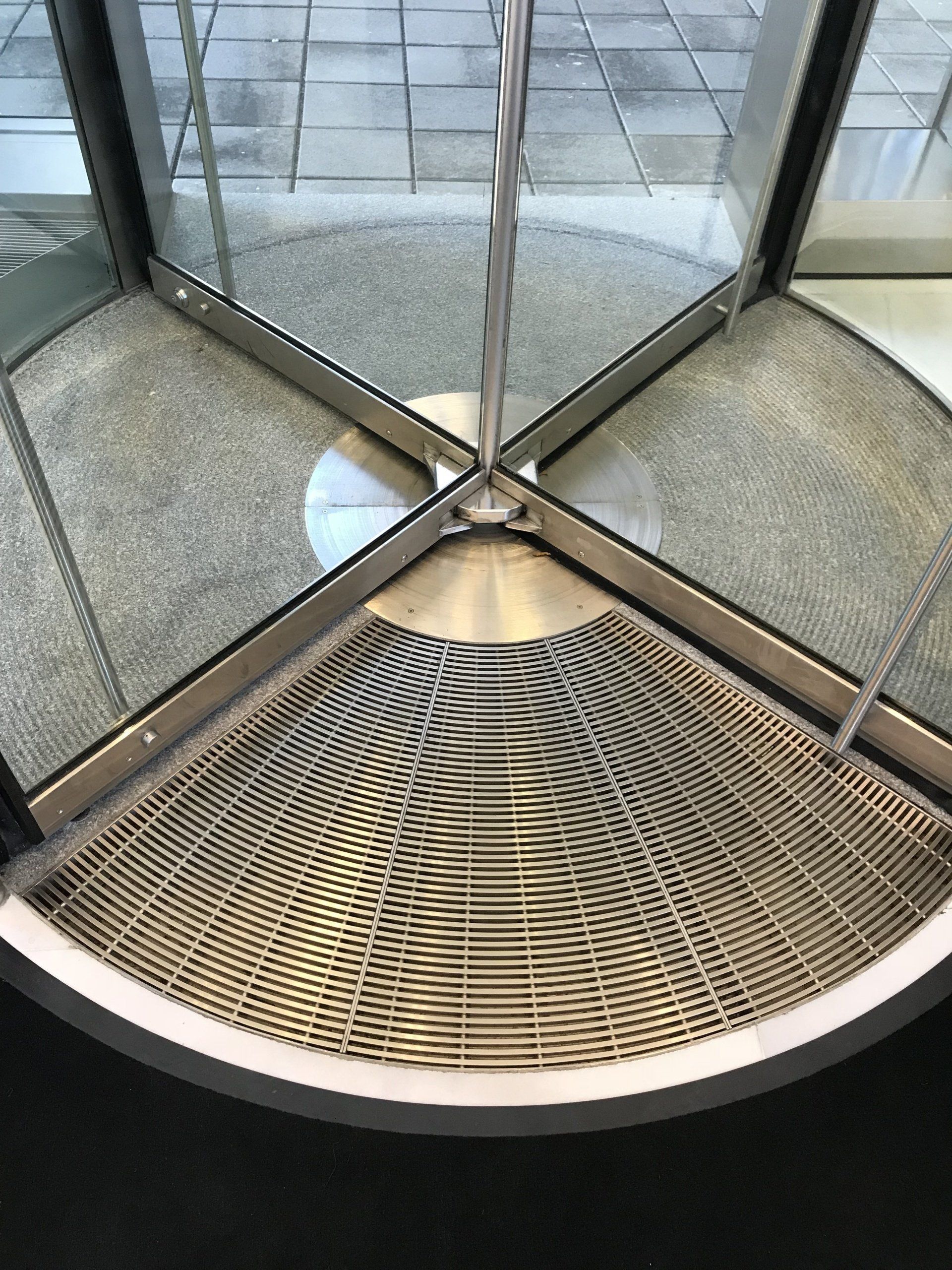 A close up of a revolving door with a metal mat on the floor.
