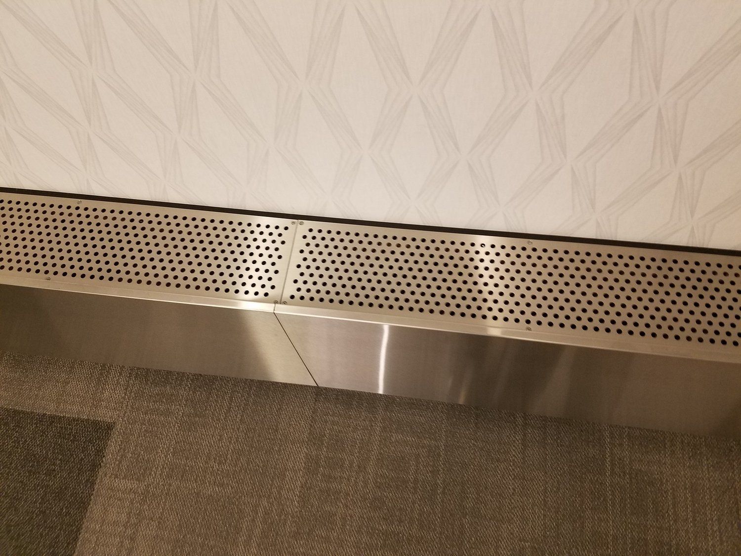 A stainless steel radiator cover is sitting on the floor next to a wall.