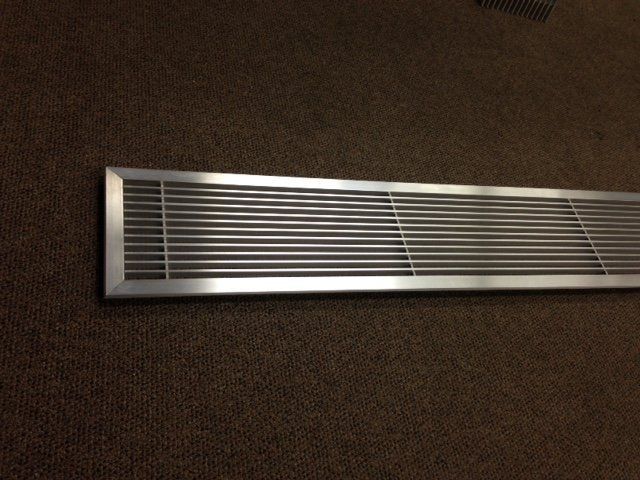 A stainless steel air vent is sitting on a brown carpet