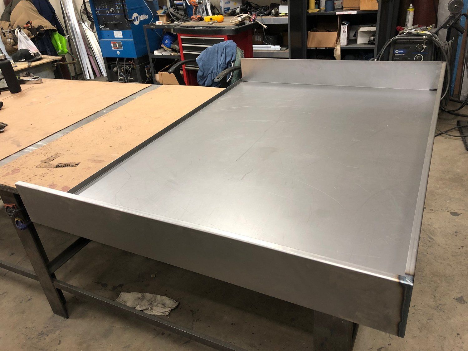 A stainless steel table is sitting on top of a wooden table in a workshop.