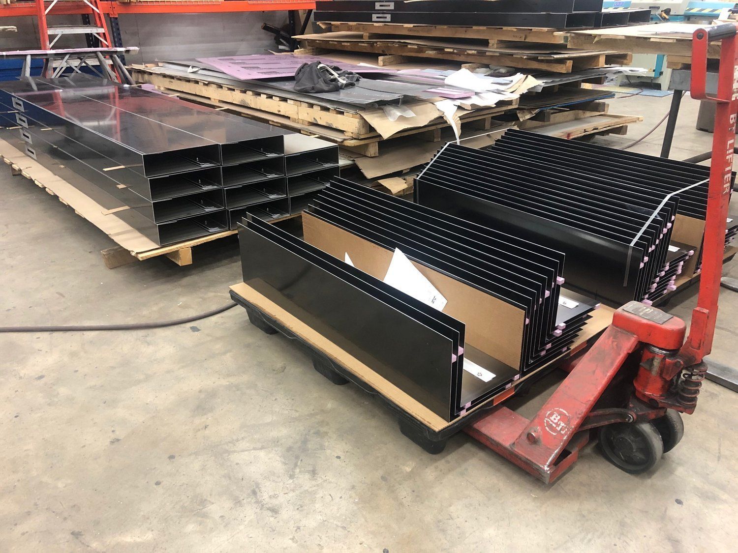 A red pallet truck is carrying a stack of black boxes