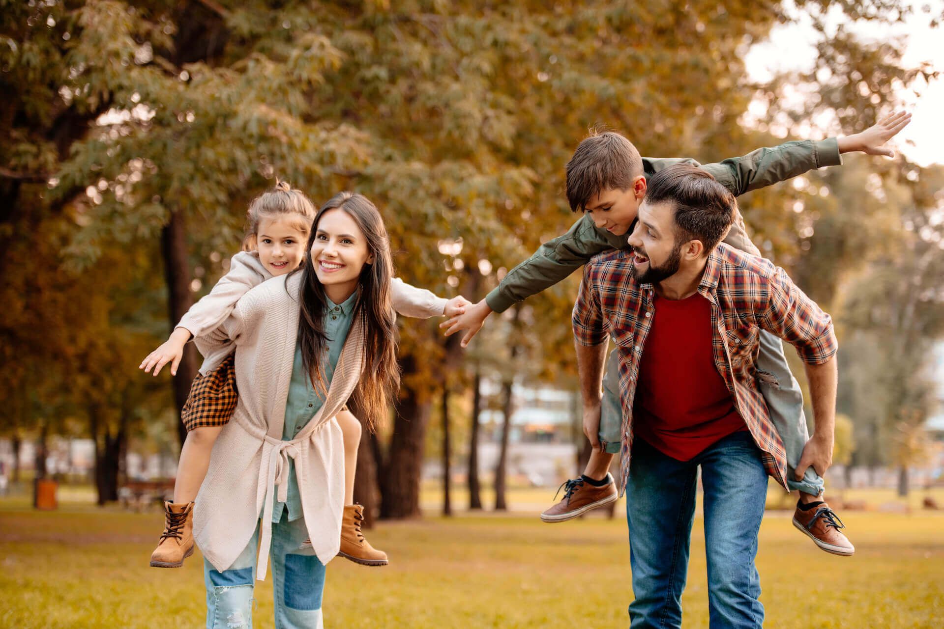 a man is carrying two children on his shoulders in a park