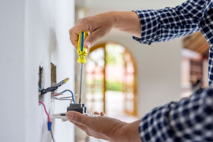 A man is installing a light switch on a wall with a screwdriver.