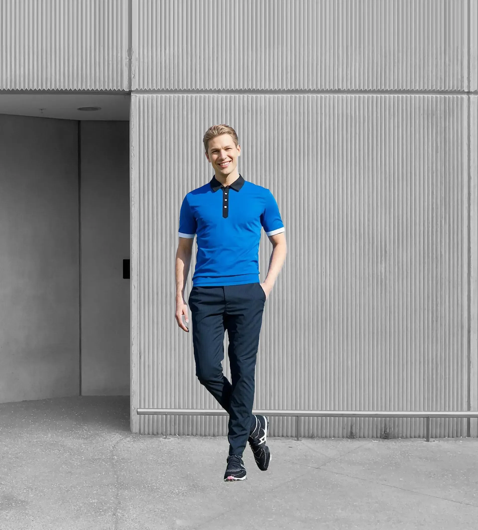 A man in a blue polo shirt and black pants is standing in front of a building.