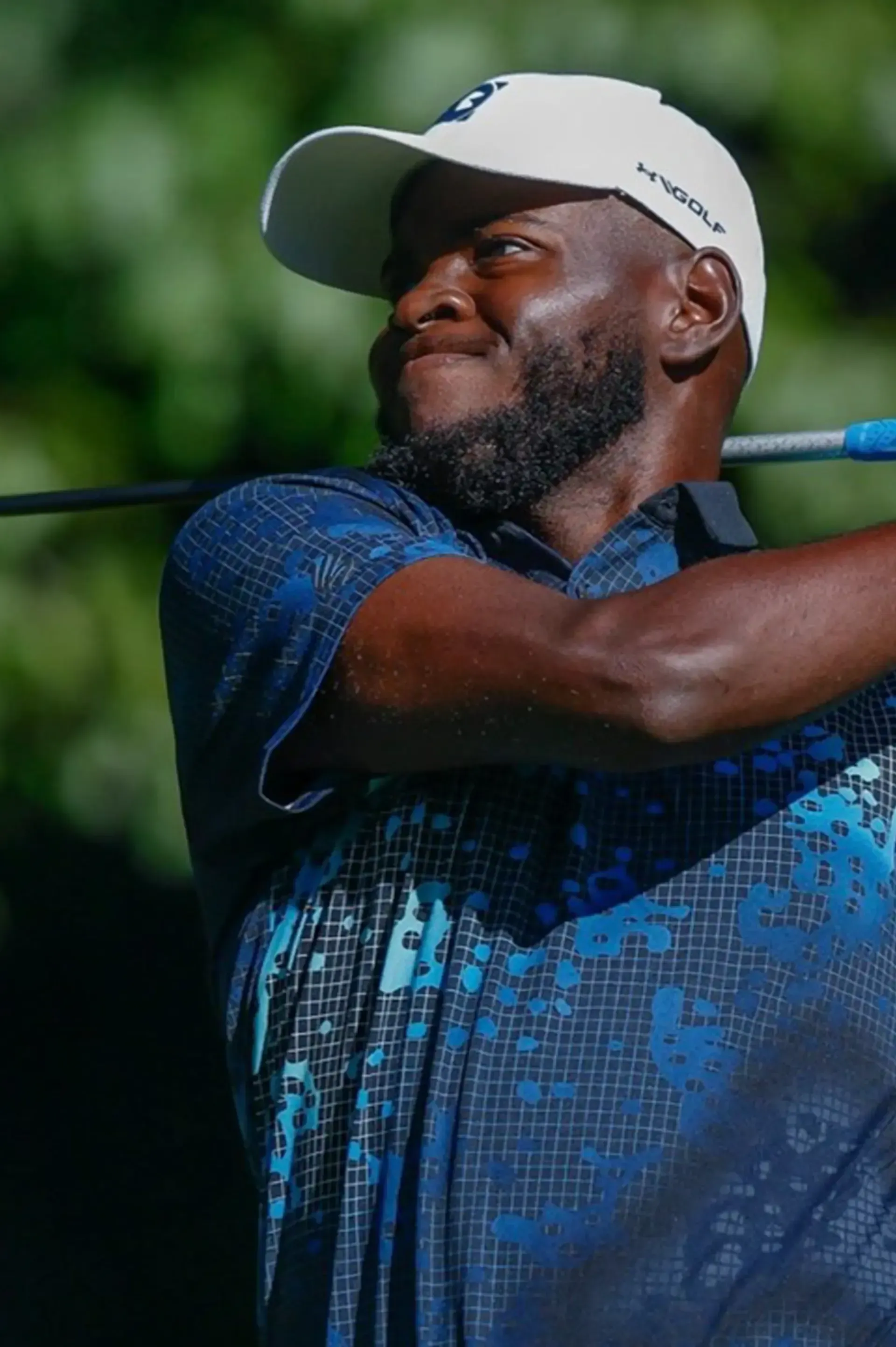 A man wearing a white hat and a blue shirt is swinging a golf club.