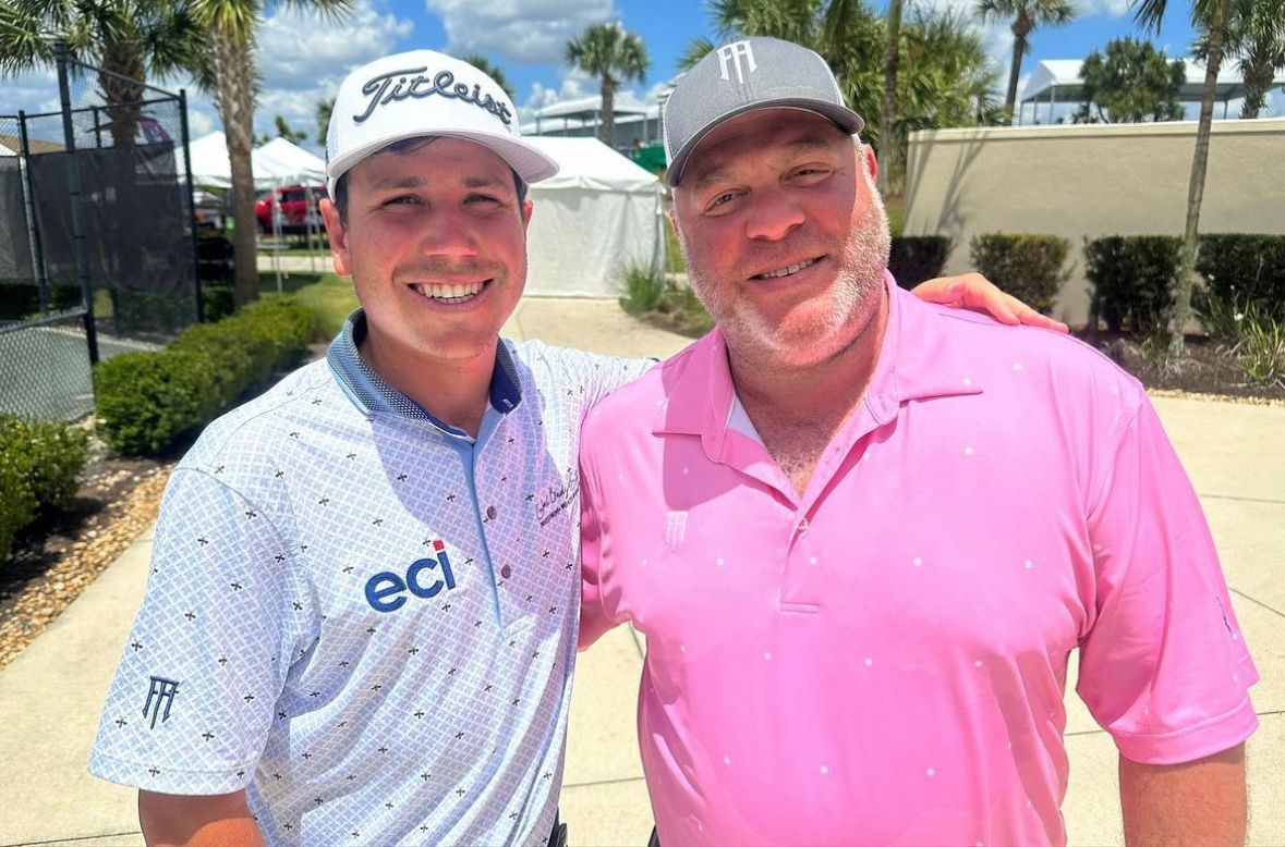 A man in a pink shirt is standing next to a man in a white shirt.
