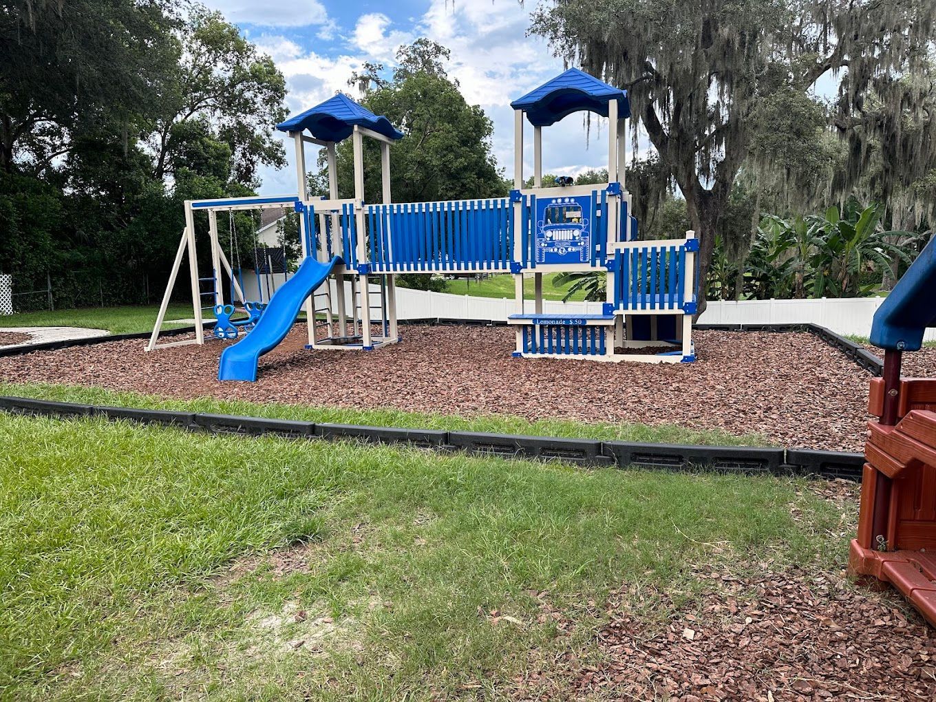 A blue and white playground with a slide and swings in a park.