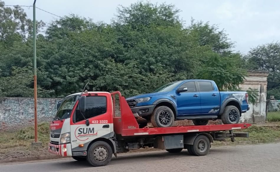 Un coche rojo está siendo remolcado por una grúa de plataforma en un paso de peatones.