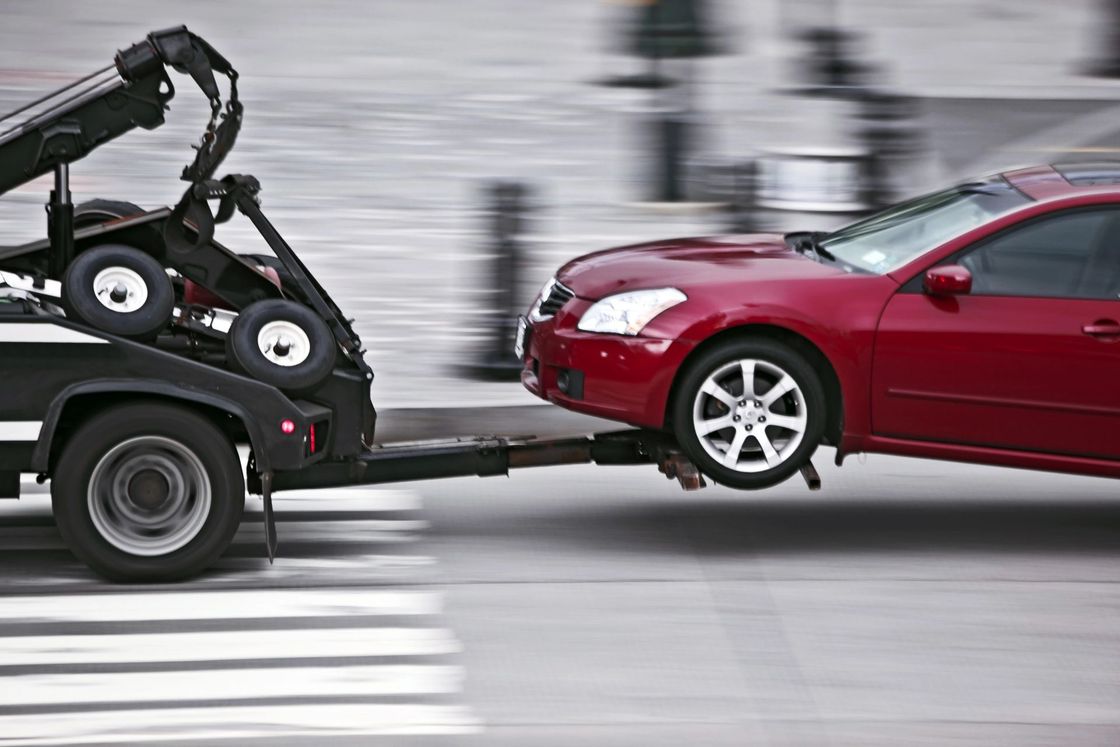 Un coche rojo está siendo remolcado por una grúa de plataforma en un paso de peatones.