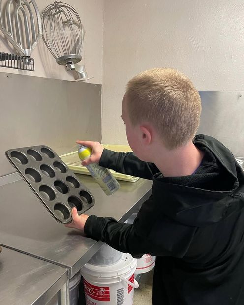 A young boy is using a spray bottle to spray a muffin pan.