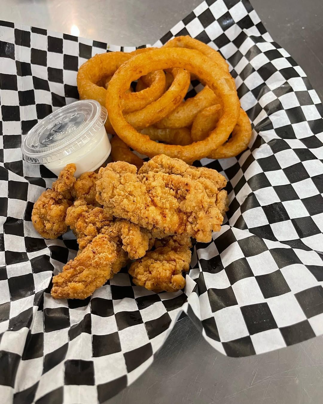 A basket of chicken tenders and onion rings on a checkered napkin.