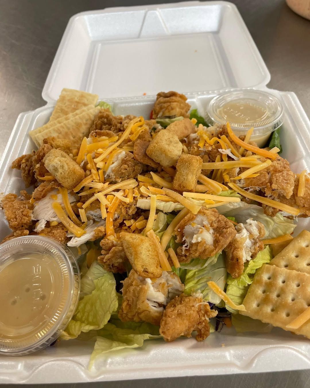 A chicken salad in a styrofoam container with crackers and dressing.