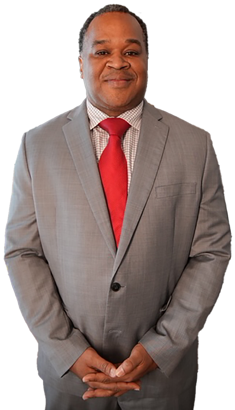 A man in a grey suit, patterned dress shirt, and red tie stands facing forward with his hands clasped against white.