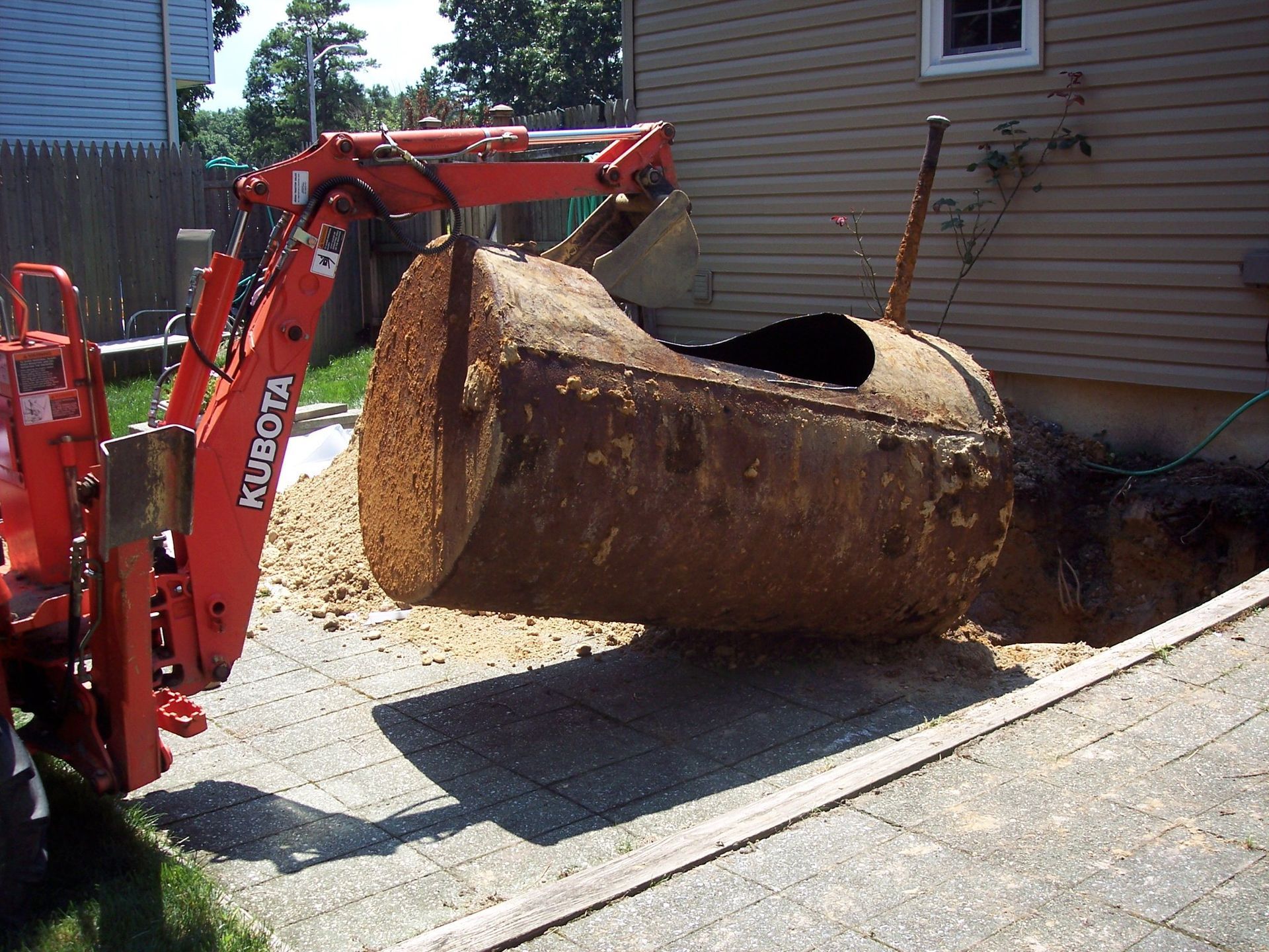 A large rusty tank is being removed by a kubota tractor