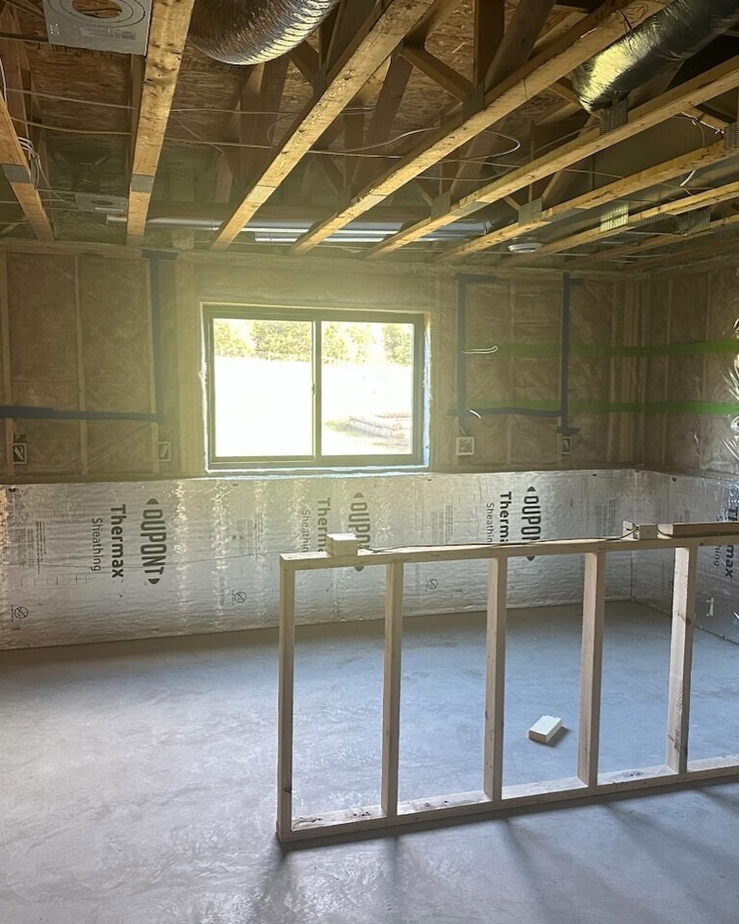 Unfinished room with exposed ceiling beams, window, and a framed wall section on a concrete floor.
