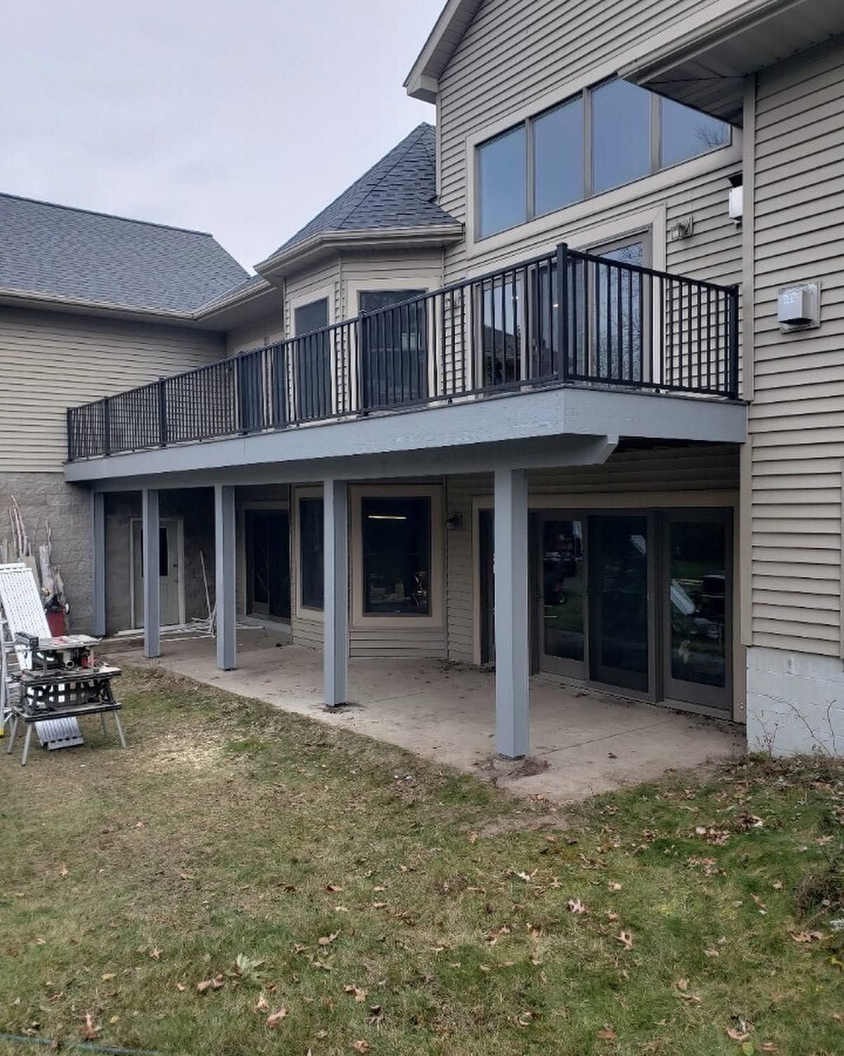 Backyard view of a two-story house with a raised deck, black railing, and covered patio below