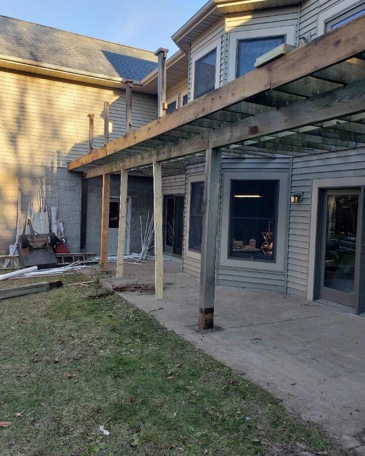 Backyard patio under construction with wooden posts, pergola beams, and a two-story house exterior.