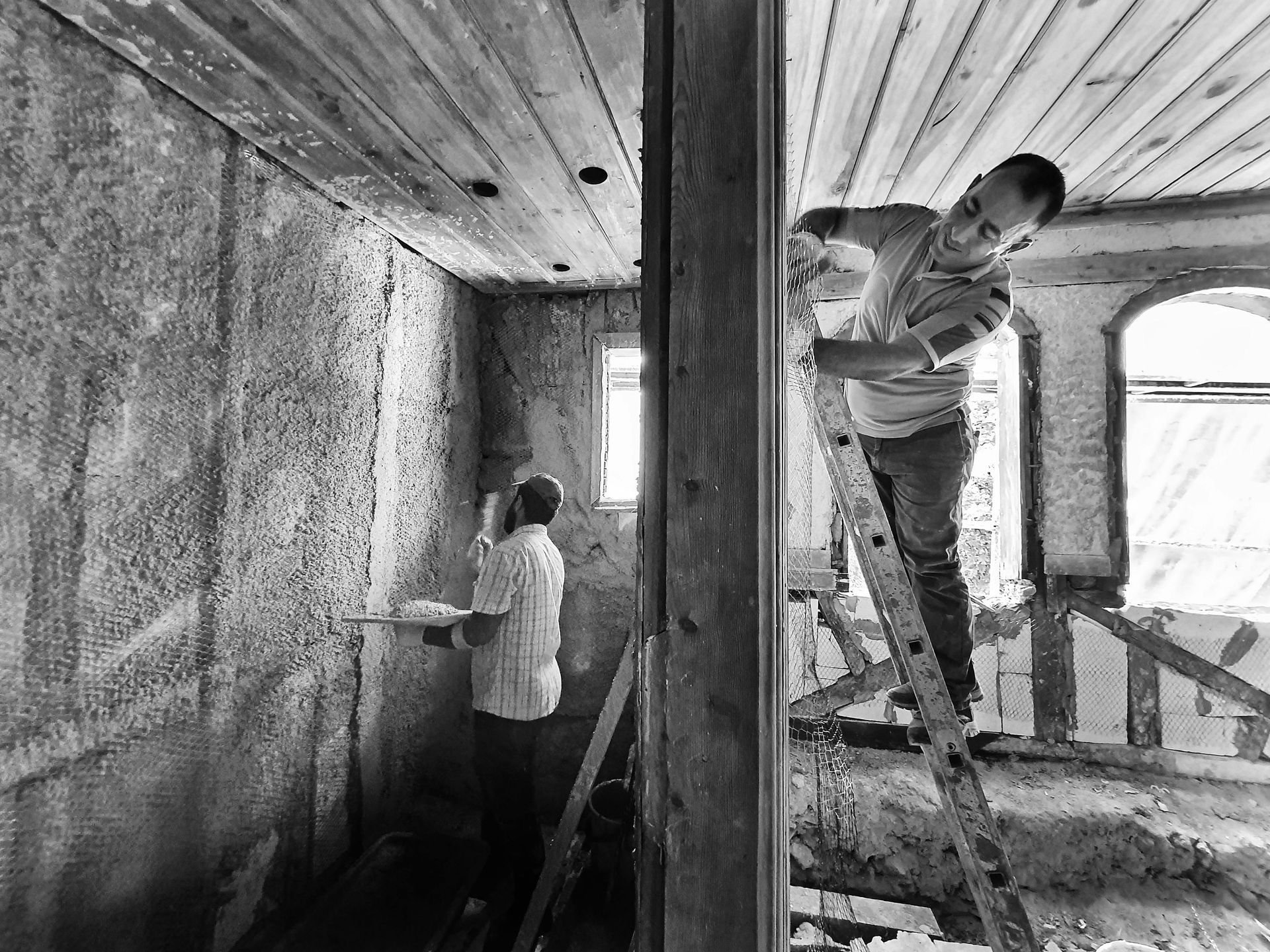 Two men renovating an interior. One on a ladder, the other applying plaster to the wall.