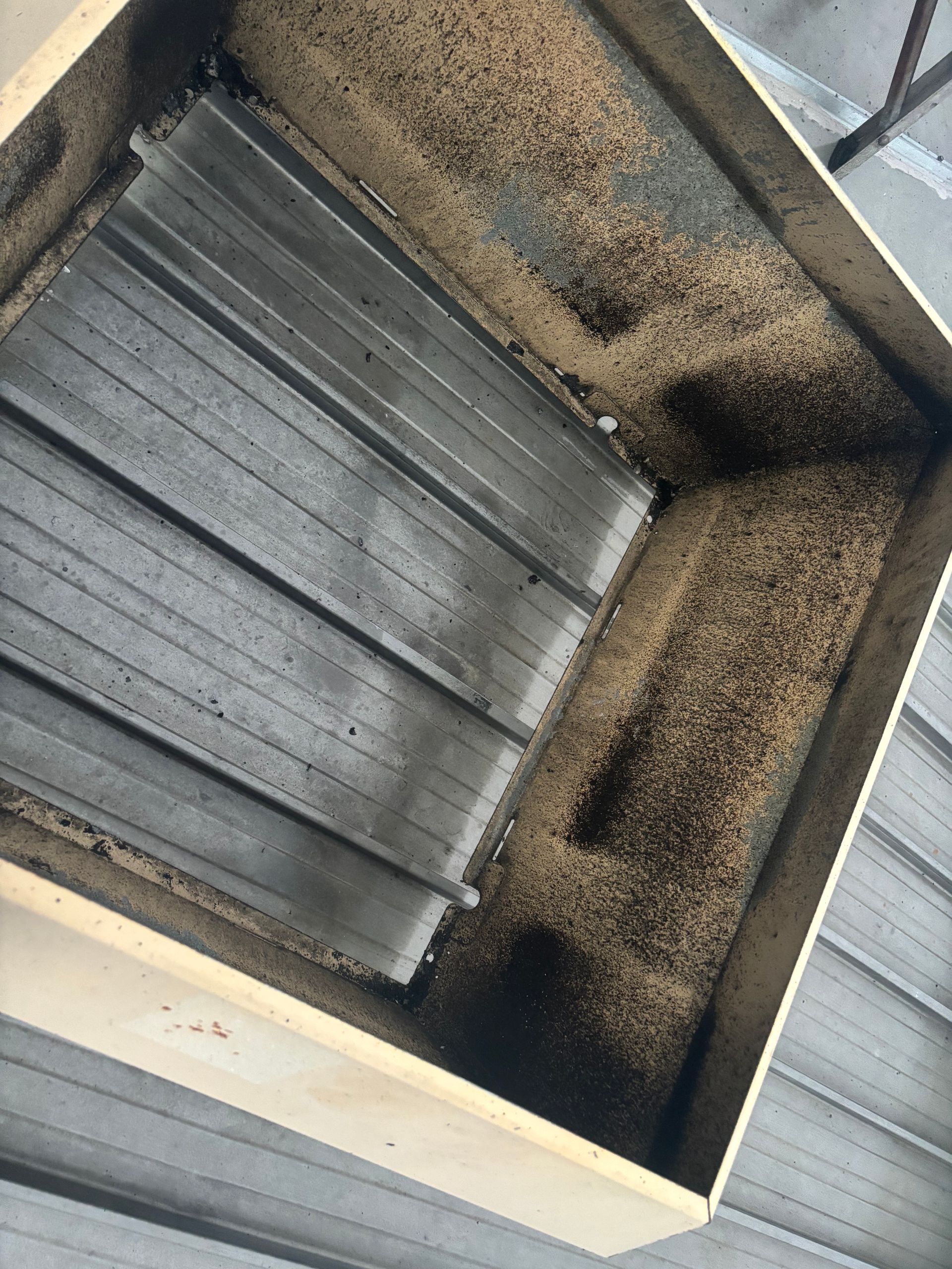 Ventilation box with accumulated debris; gray metal slats, tan frame, outdoor setting.  DM & MM Services, Exhaust Cleaning, Townsville, QLD.