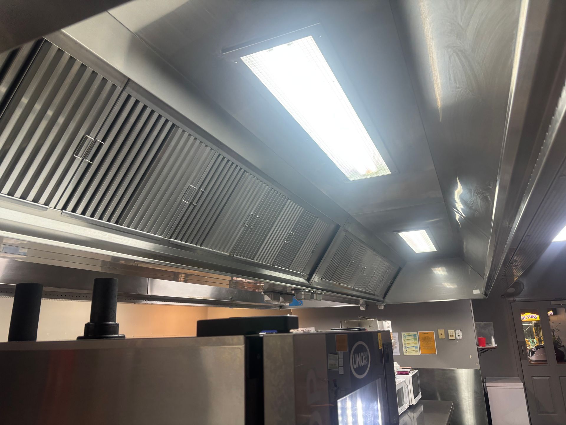 Stainless steel commercial kitchen exhaust hood with overhead lighting.— DM & MM Services Pty Ltd in Ayr, QLD
