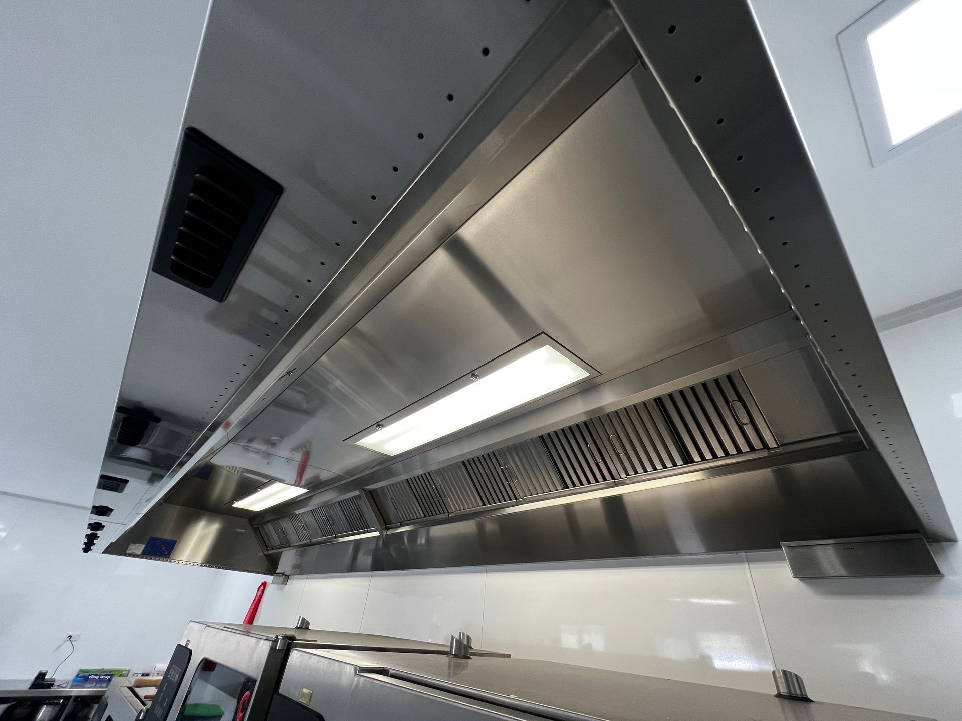 A Stainless Steel Hood is Hanging From the Ceiling in a Kitchen — DM & MM Services Pty Ltd in Ingham, QLD