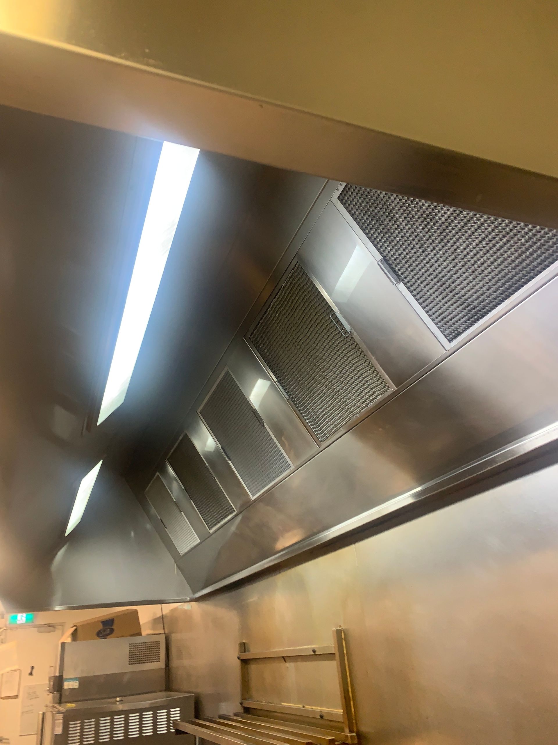 A Stainless Steel Hood Is Hanging From The Ceiling Of A Kitchen — DM & MM Services Pty Ltd in Mount Louisa, QLD