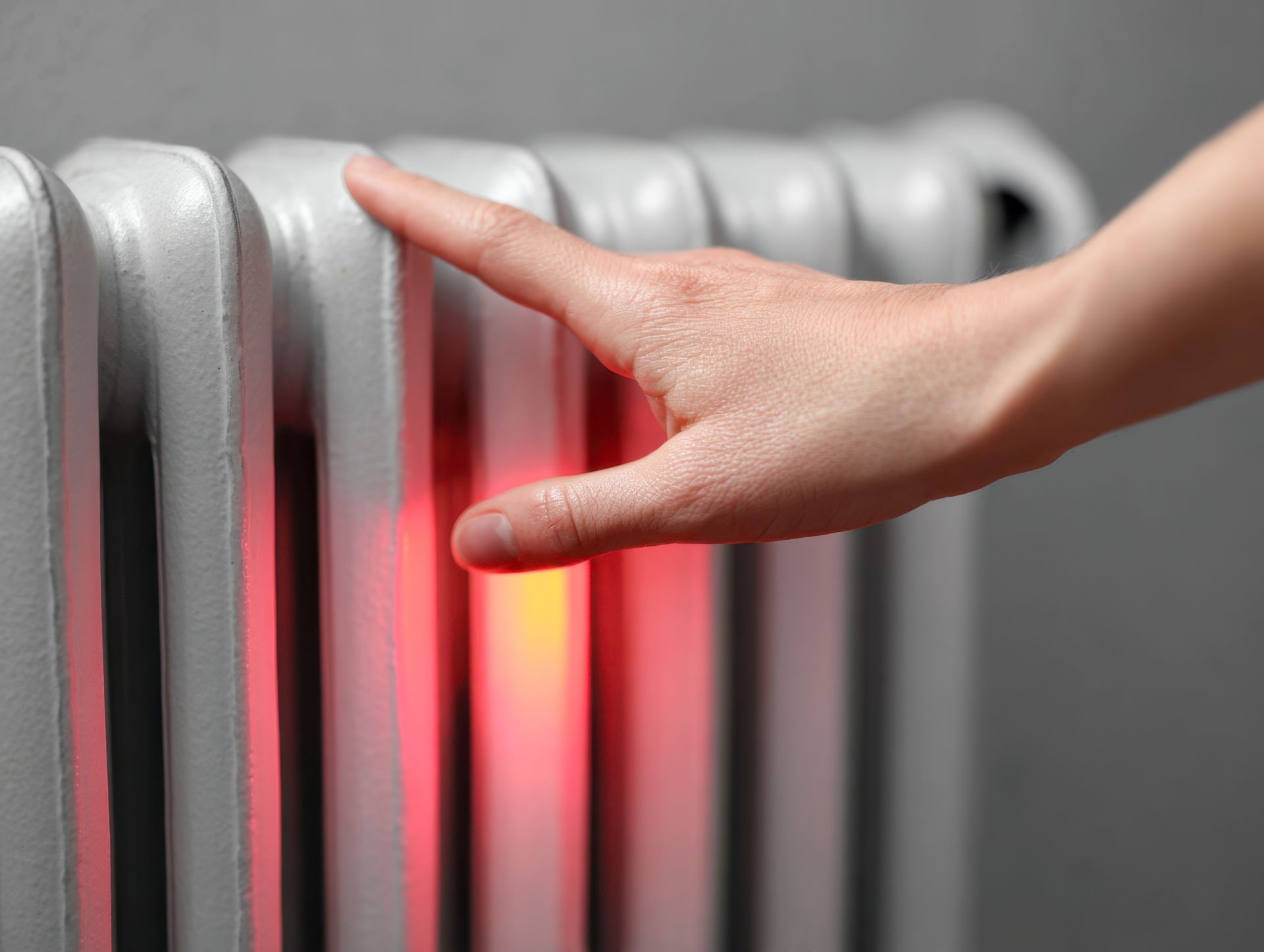 A hand handles the heating valve of a heating radiator.