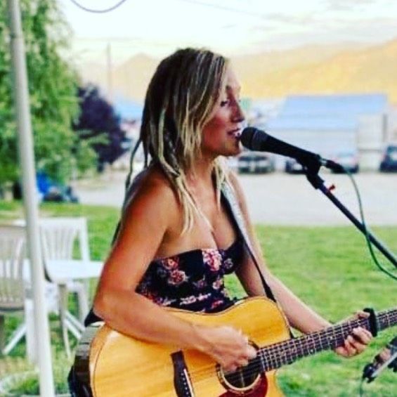 A woman singing into a microphone while holding a guitar