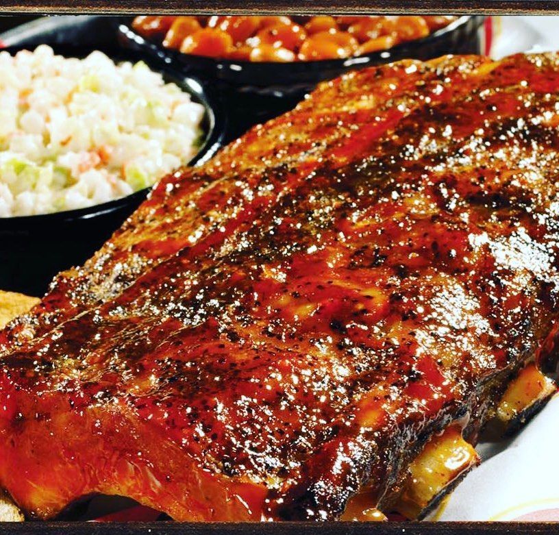 A close up of ribs on a plate with coleslaw and baked beans
