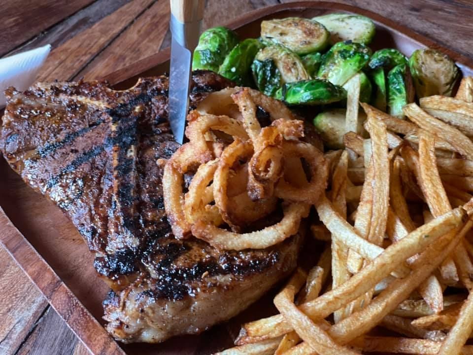 A steak and french fries on a wooden plate on a wooden table.