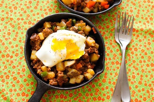 A skillet filled with meat and vegetables with an egg on top.