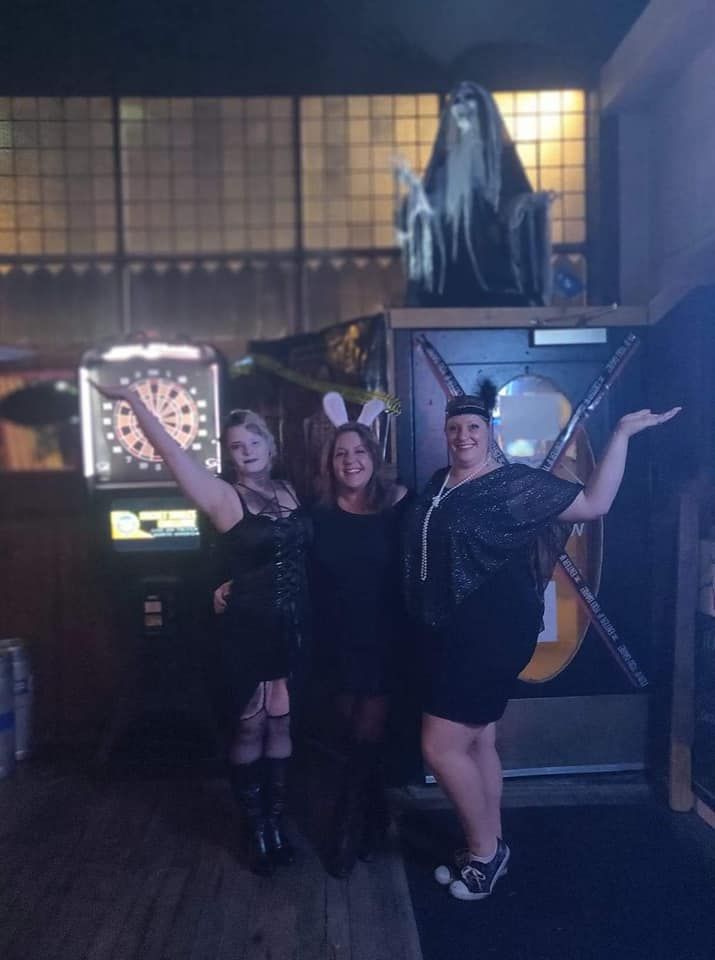 Three women are posing for a picture in front of a dart board.