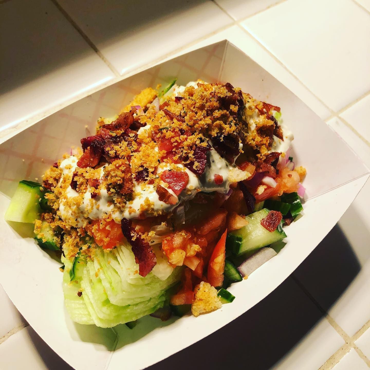 A salad in a paper container on a tiled counter top