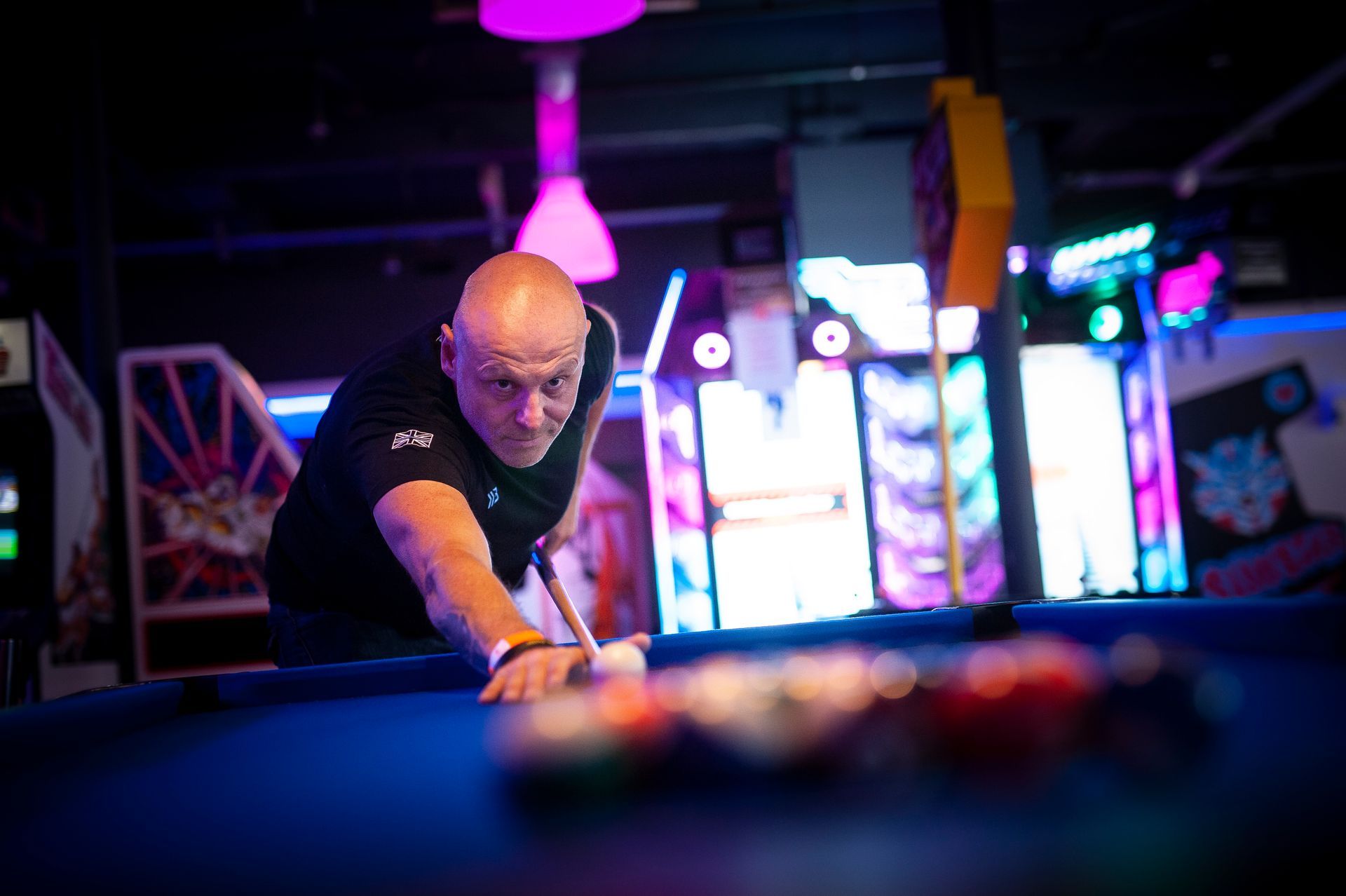 A man is playing pool on a pool table in an arcade.