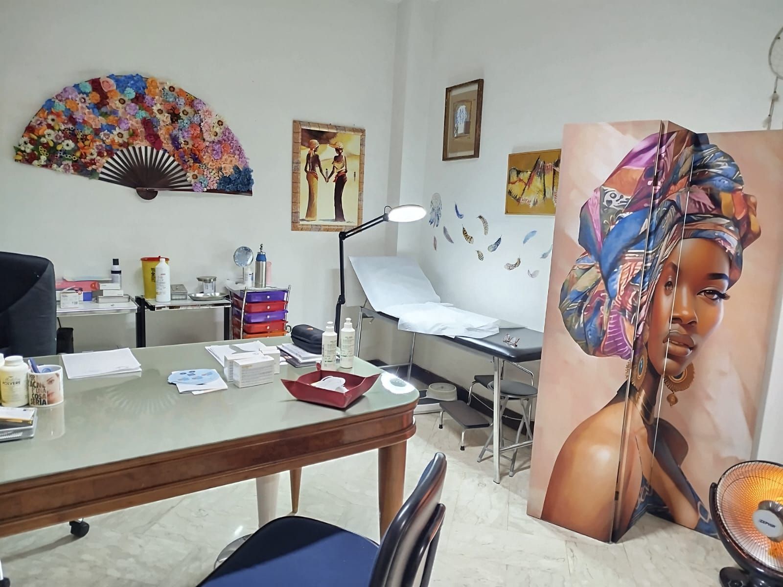 Interno di uno studio medico con tavolo da visita, scrivania e un'opera d'arte raffigurante una donna con un copricapo.