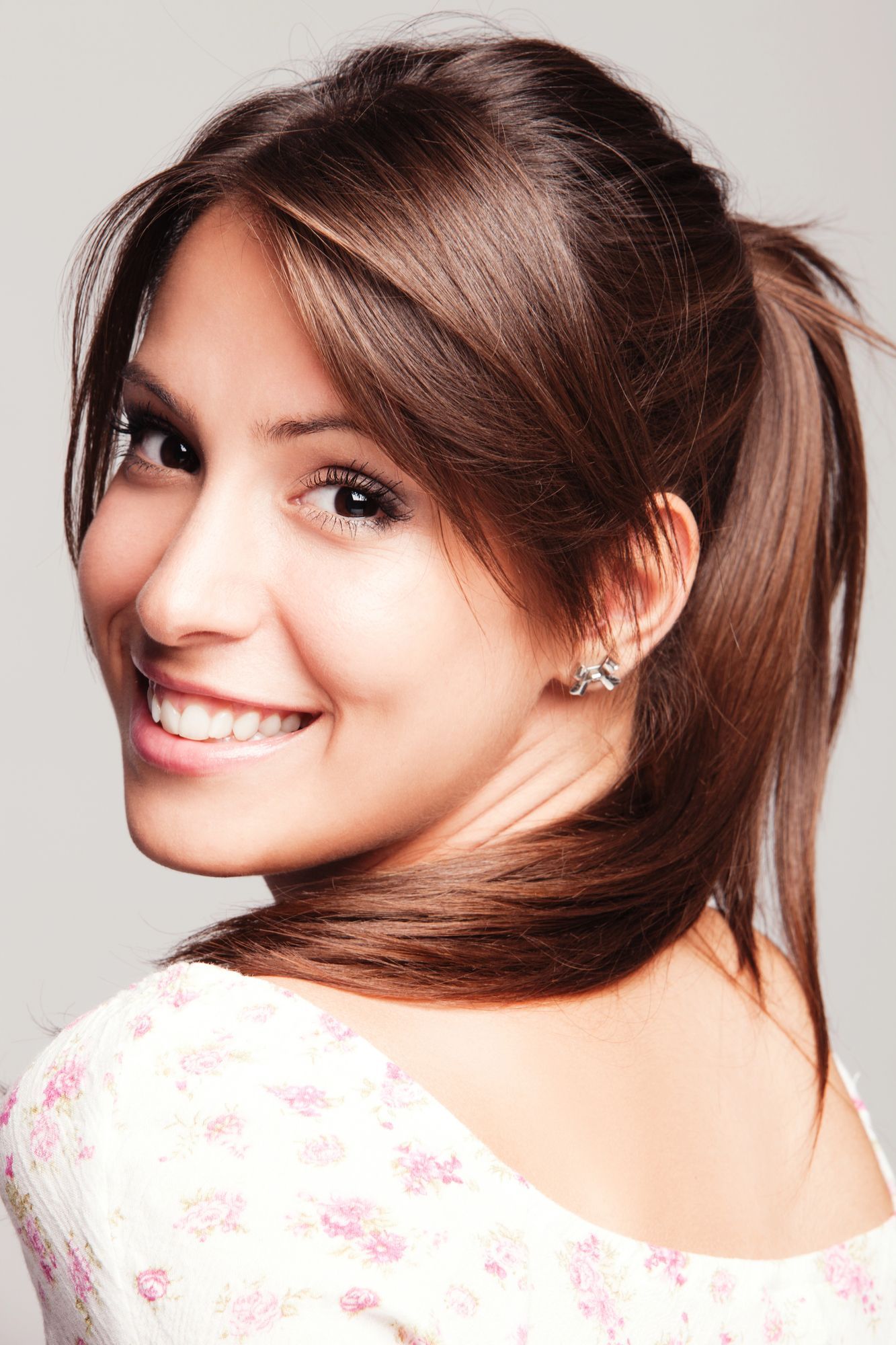 Una donna con i capelli castani raccolti in una coda di cavallo sorride, guardandosi alle spalle.